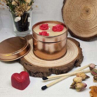 MysticGlow handmade soy candle in bronze tin with red rose wax embeds, displayed on rustic wood slice with dried flowers and matches