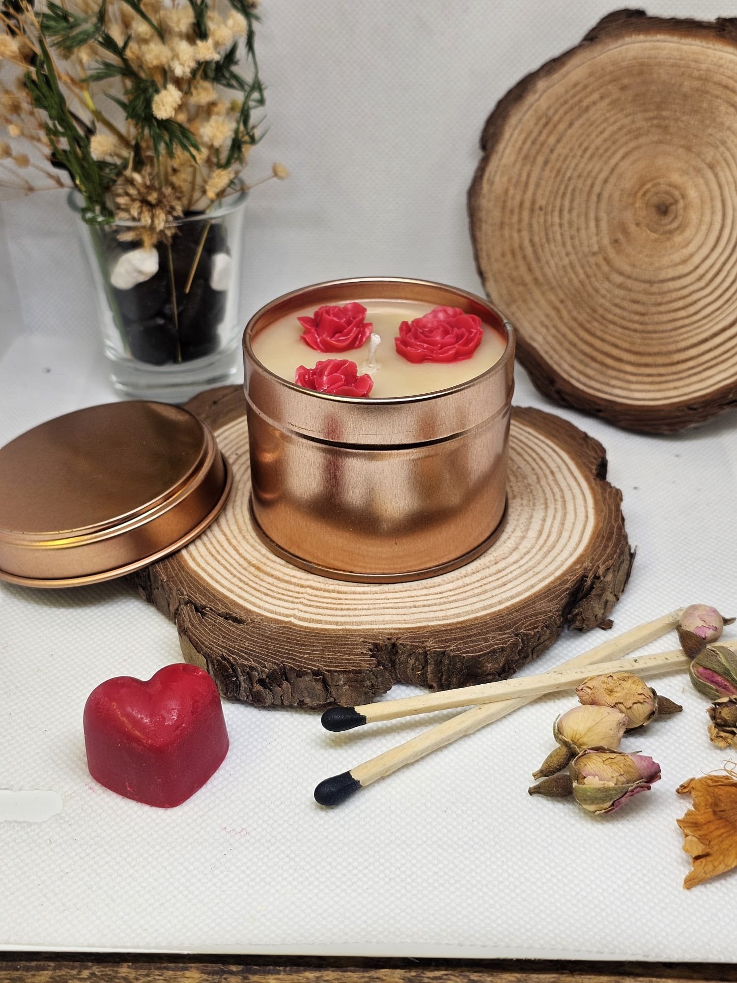 MysticGlow handmade soy candle in bronze tin with red rose wax embeds, displayed on rustic wood slice with dried flowers and matches