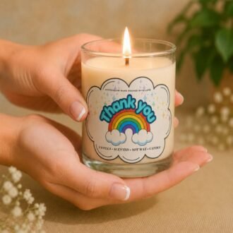 MysticGlow handmade vanilla scented soy wax Thank You candle in a clear glass jar, featuring a colourful rainbow and clouds label, held gently in hands with a glowing flame. A thoughtful appreciation gift.